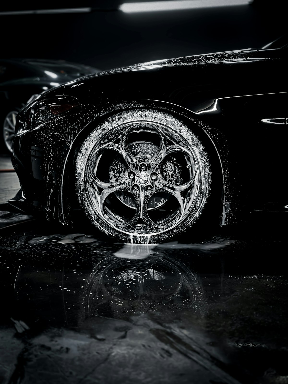 Close-up of a soapy wheel and glossy black car panel reflecting a garage light
